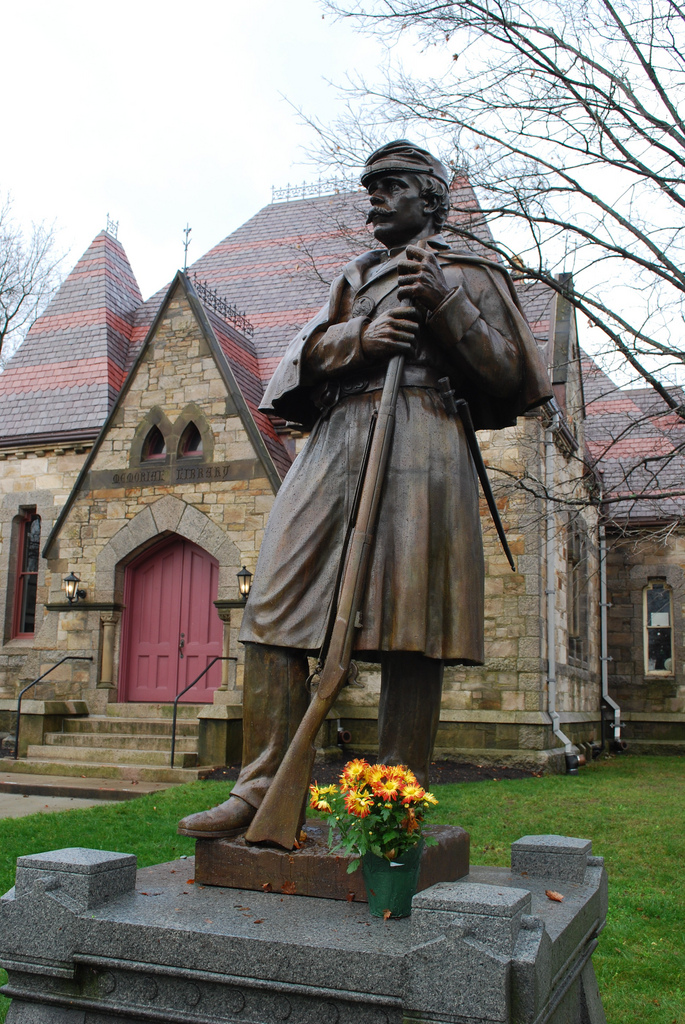 view of a statue of a soldier with an historic building made of large stones with a red roof behind 